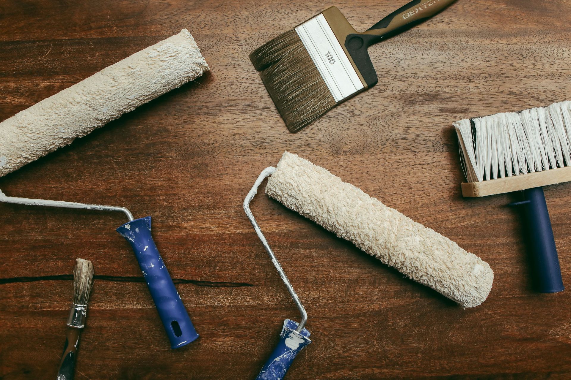 Top view of various painting tools including rollers and brushes laid out on a wooden surface.